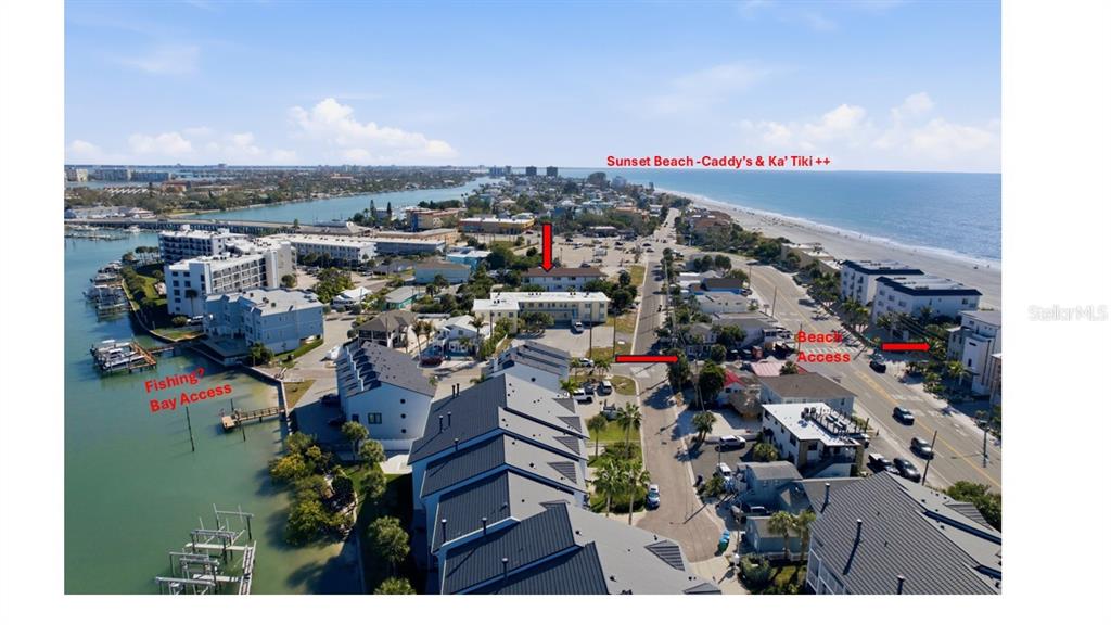 An aerial view shows a coastal neighborhood with bay access, beach access, and nearby buildings — 9895 1ST STREET E UNIT 9, TREASURE ISLAND, FL