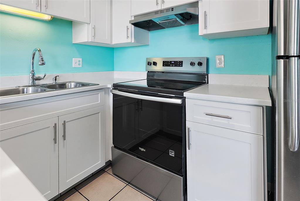 A kitchen features white cabinets, a stainless steel stove, and bright turquoise walls — 9895 1ST STREET E UNIT 9, TREASURE ISLAND, FL