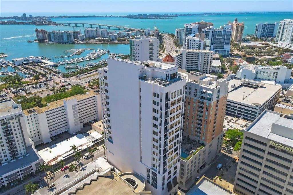 An aerial view shows a tall white residential building surrounded by city high-rises and water — 33 S PALM AVENUE UNIT 1503, SARASOTA, FL