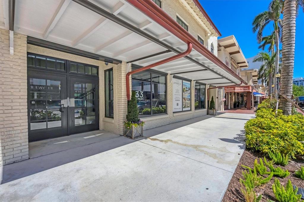 The exterior of a commercial building features a covered walkway, brick walls, and glass doors — 33 S PALM AVENUE UNIT 1503, SARASOTA, FL
