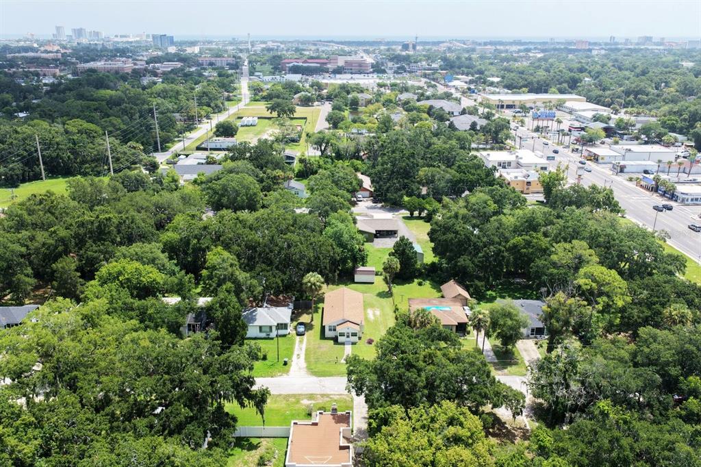 An aerial view shows a suburban neighborhood with houses, dense trees, and a nearby road — 125 N CAROLINE STREET, DAYTONA BEACH, FL