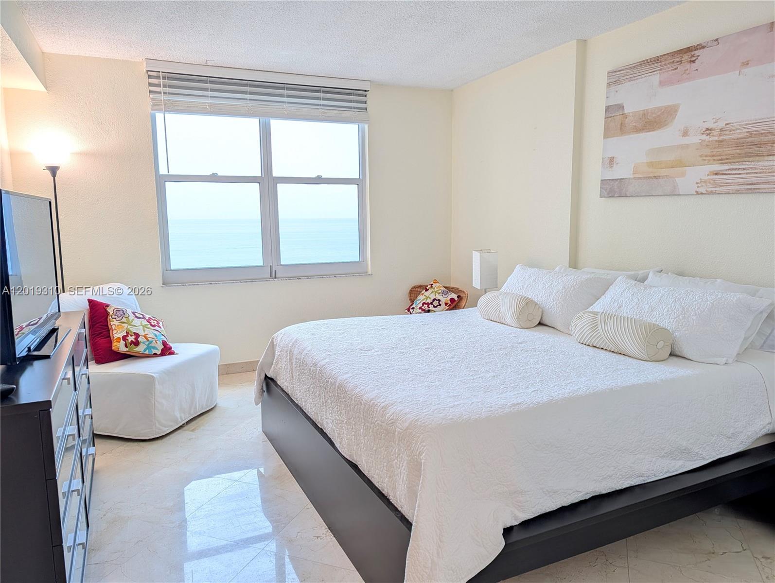 A bedroom features a bed, a white chair, a dresser, and a view of the ocean — 2501 S Ocean Dr # 1021, Hollywood FL 33019, HOLLYWOOD, FL