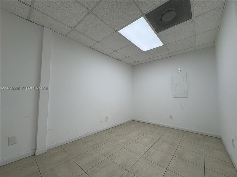 An empty office room features white walls, a tiled floor, and a drop ceiling — MIAMI, FL