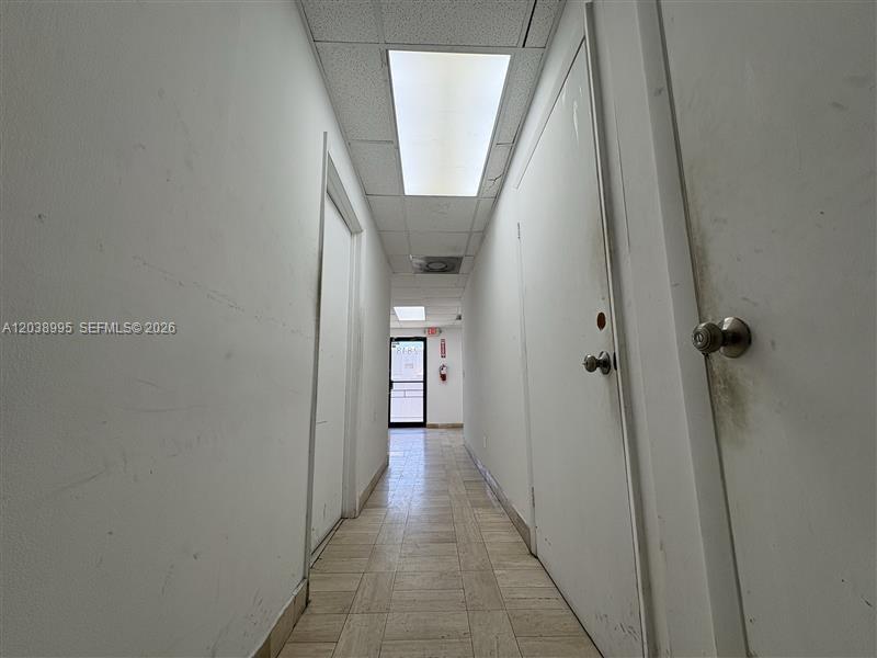 A narrow hallway with white walls, tiled flooring, and several closed doors leads to an exit — MIAMI, FL