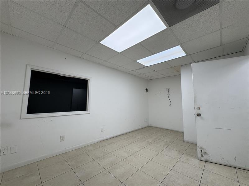 An empty office room features white walls, a drop ceiling, and light-colored tile flooring — MIAMI, FL