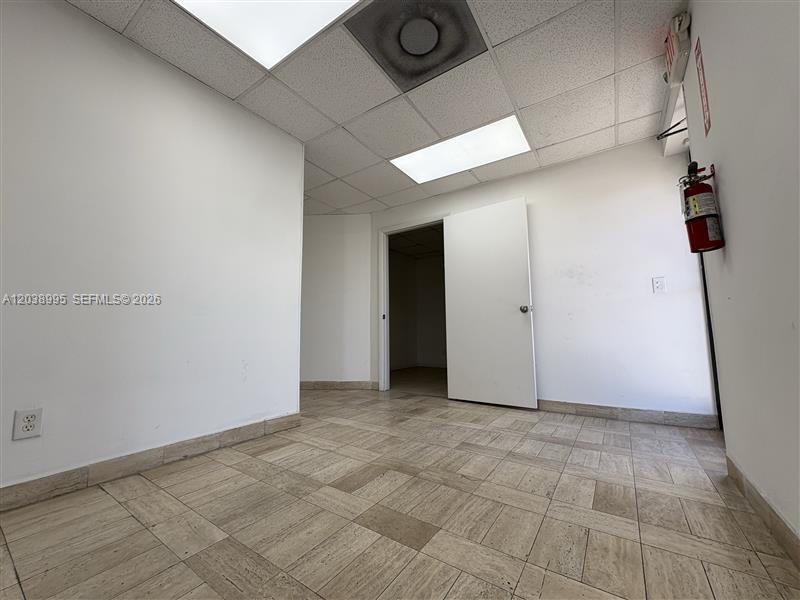 An empty office room features white walls, a tiled floor, and a drop ceiling — MIAMI, FL