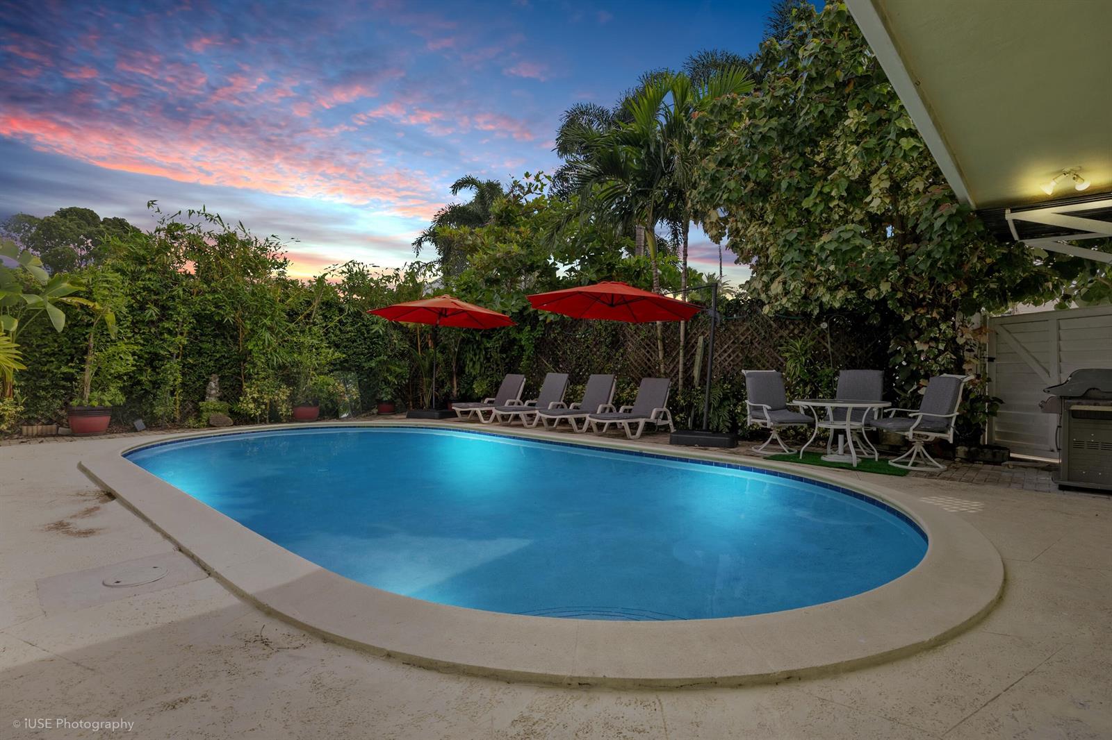 A backyard swimming pool with lounge chairs and umbrellas under a sunset sky — 1250 Arthur Street, Hollywood FL 33019, HOLLYWOOD, FL