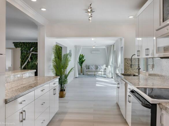 A modern kitchen with white cabinets and granite countertops opens into a bright living area — 1250 Arthur Street, Hollywood FL 33019, HOLLYWOOD, FL
