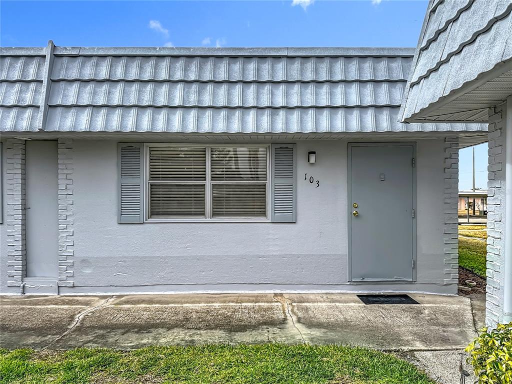 The exterior of a single-story residential unit features a gray door, a window, and siding — 202 BEDFORD TRAIL UNIT 103, SUN CITY CENTER, FL