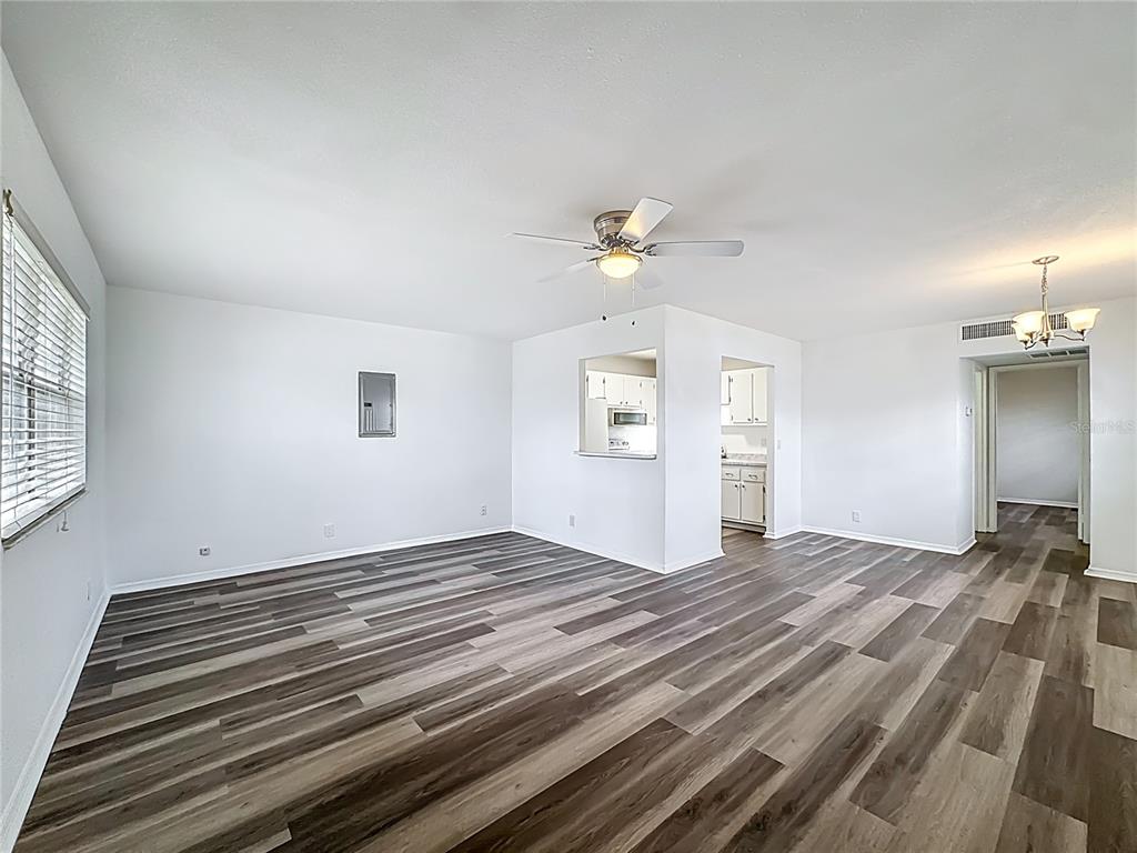 An empty living room features wood-look vinyl flooring, white walls, a ceiling fan, and a pass-through — 202 BEDFORD TRAIL UNIT 103, SUN CITY CENTER, FL