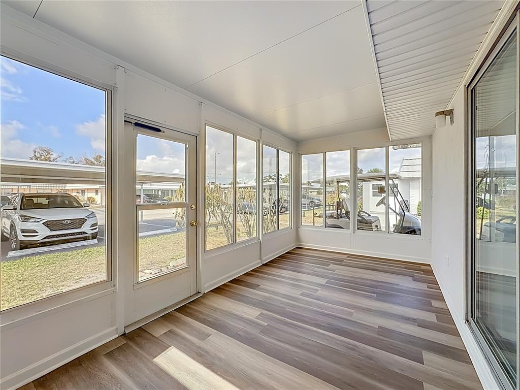 A sunroom with wood-look flooring, white walls, and large windows overlooking a parking area — 202 BEDFORD TRAIL UNIT 103, SUN CITY CENTER, FL