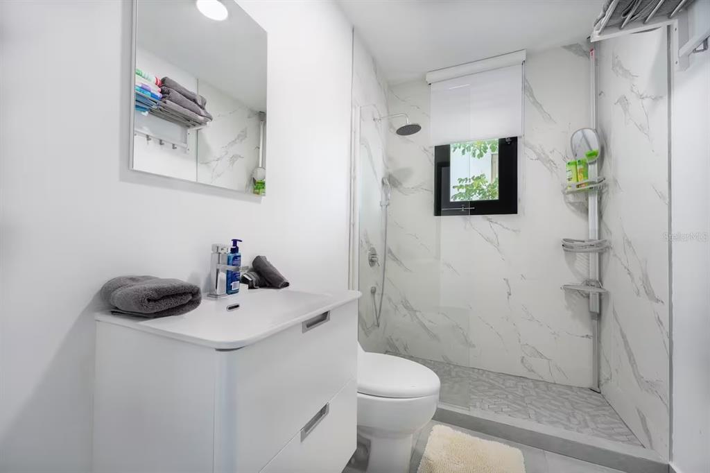 A modern bathroom features a white vanity, a toilet, and a marble-tiled walk-in shower — 149 CALLE DELBREY, SAN JUAN, PR