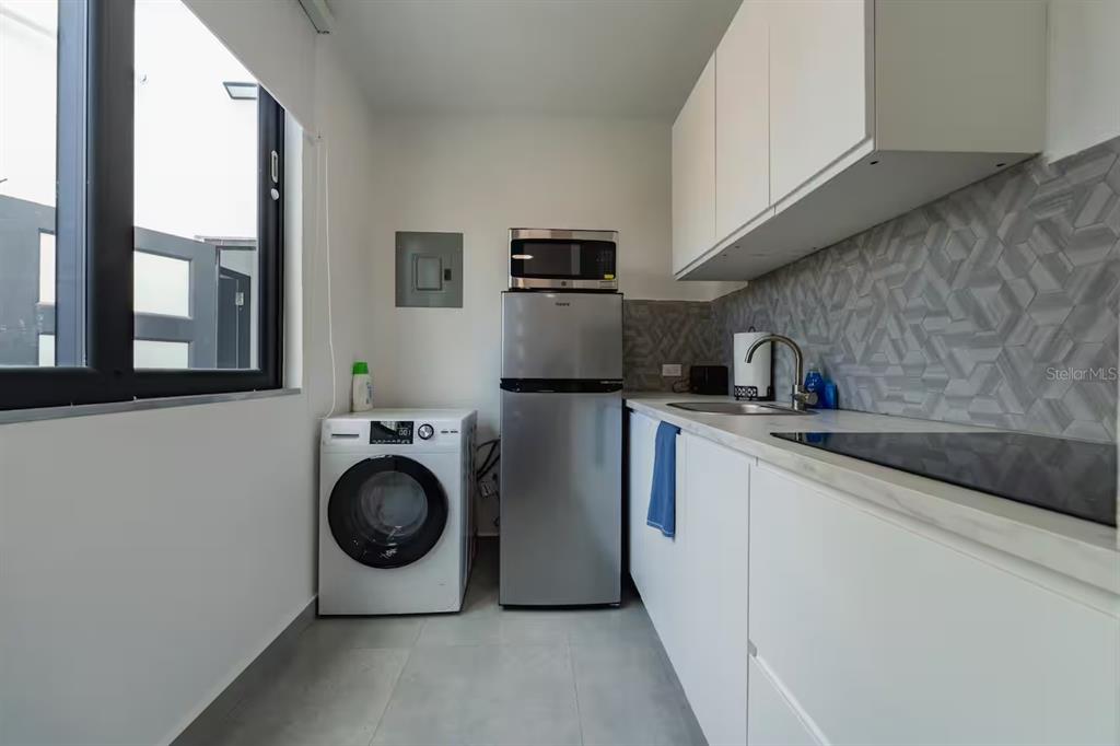 A modern kitchen features white cabinetry, stainless steel appliances, a washing machine, and gray tile — 149 CALLE DELBREY, SAN JUAN, PR