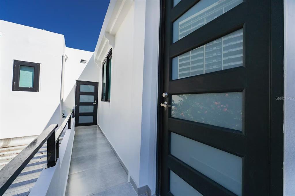 A narrow outdoor walkway with white tile flooring leads to two modern dark-framed glass doors — 149 CALLE DELBREY, SAN JUAN, PR