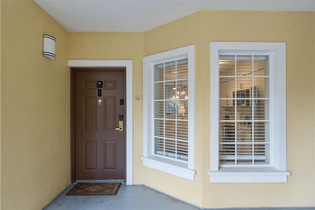 A brown front door sits next to two large windows on a yellow exterior porch — 8774 WORLDQUEST BOULEVARD UNIT 7103, ORLANDO, FL