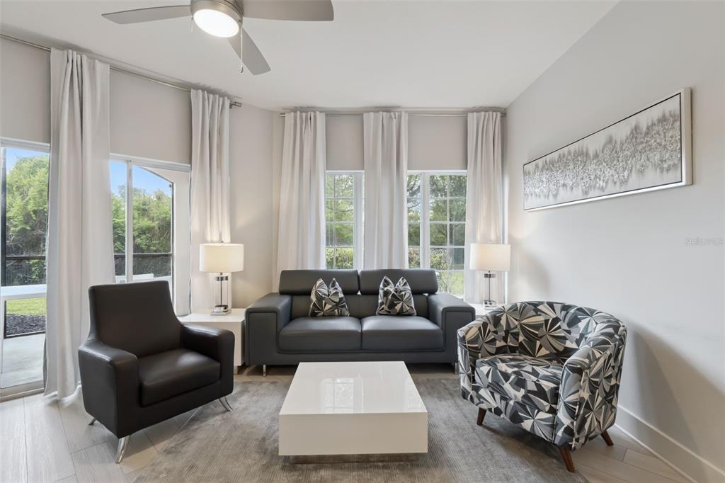 A living room features a gray sofa, two armchairs, a white coffee table, and windows — 8774 WORLDQUEST BOULEVARD UNIT 7103, ORLANDO, FL