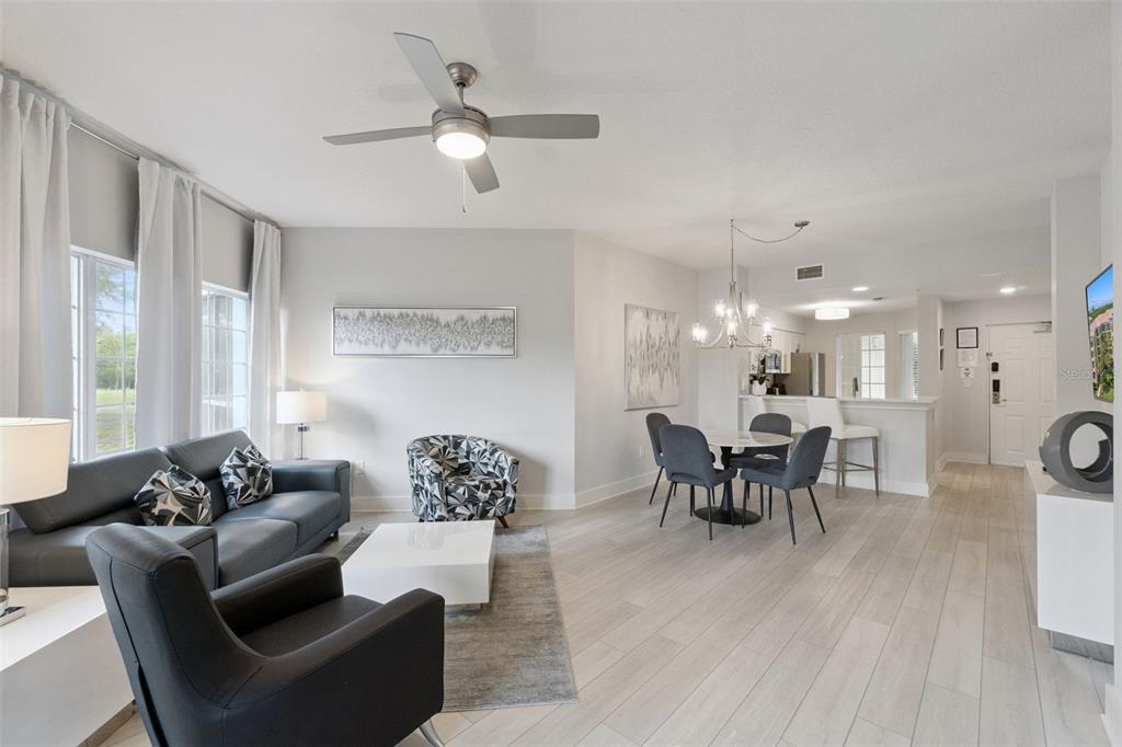 A modern living and dining area features light wood floors, gray furniture, and a ceiling fan — 8774 WORLDQUEST BOULEVARD UNIT 7103, ORLANDO, FL