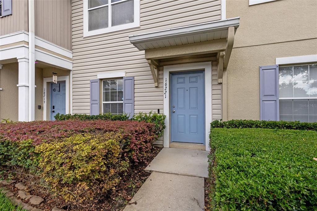 The exterior of a townhouse features a blue front door, beige siding, and trimmed hedges — 16221 SWAN VIEW CIRCLE, ODESSA, FL