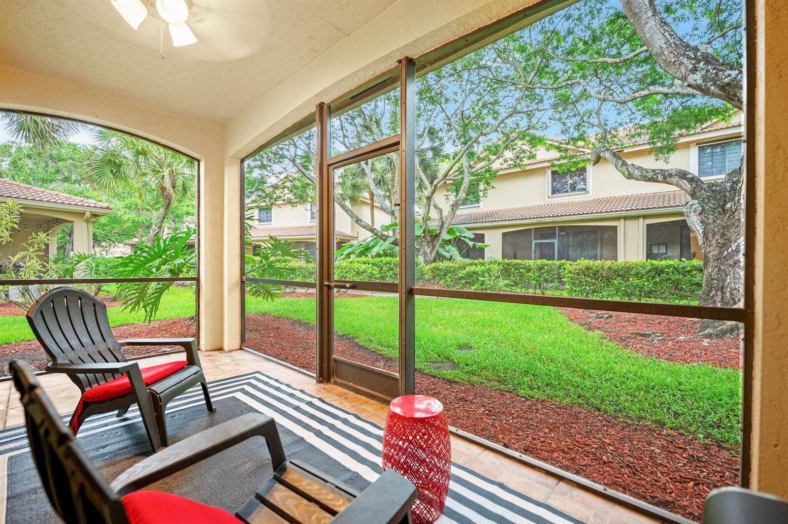 A screened-in patio with two chairs, a red side table, and a view of landscaping — 4212 Vineyard Circle, Weston FL 33332, WESTON, FL