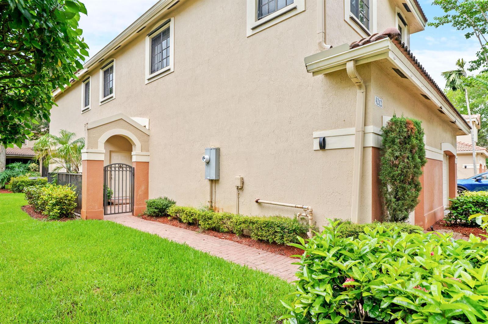 A beige two-story townhouse exterior features a brick walkway, a gated entrance, and landscaping — 4212 Vineyard Circle, Weston FL 33332, WESTON, FL