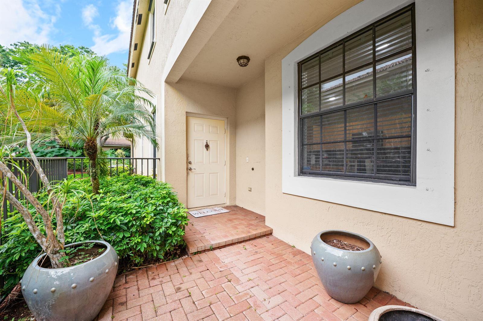 A beige stucco home entrance features a brick walkway, a front door, and potted plants — 4212 Vineyard Circle, Weston FL 33332, WESTON, FL