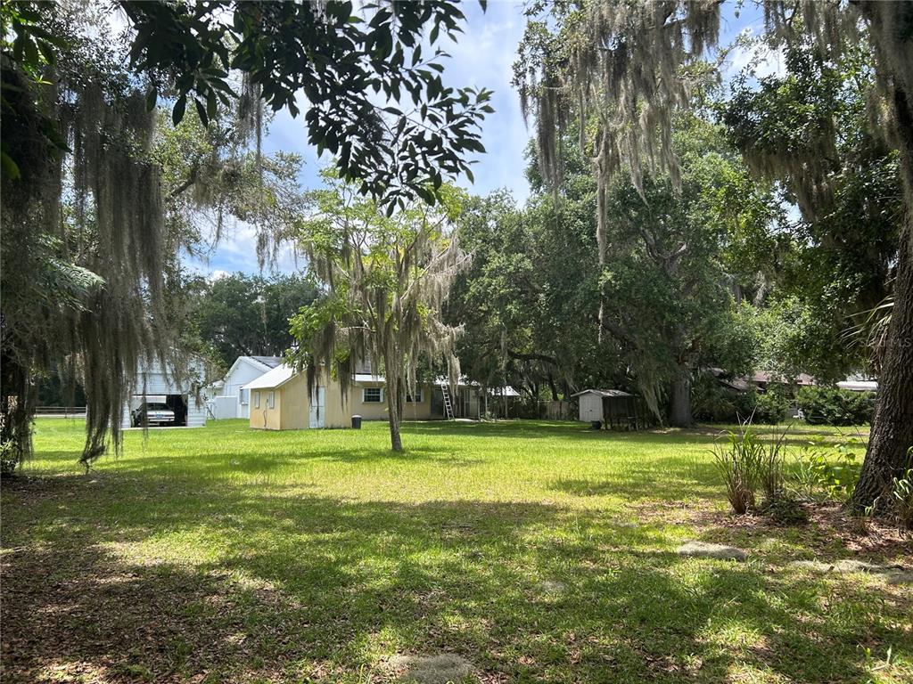 A large, grassy backyard features a yellow house, a detached garage, and mature oak trees — 1671 FORD ROAD, MIMS, FL