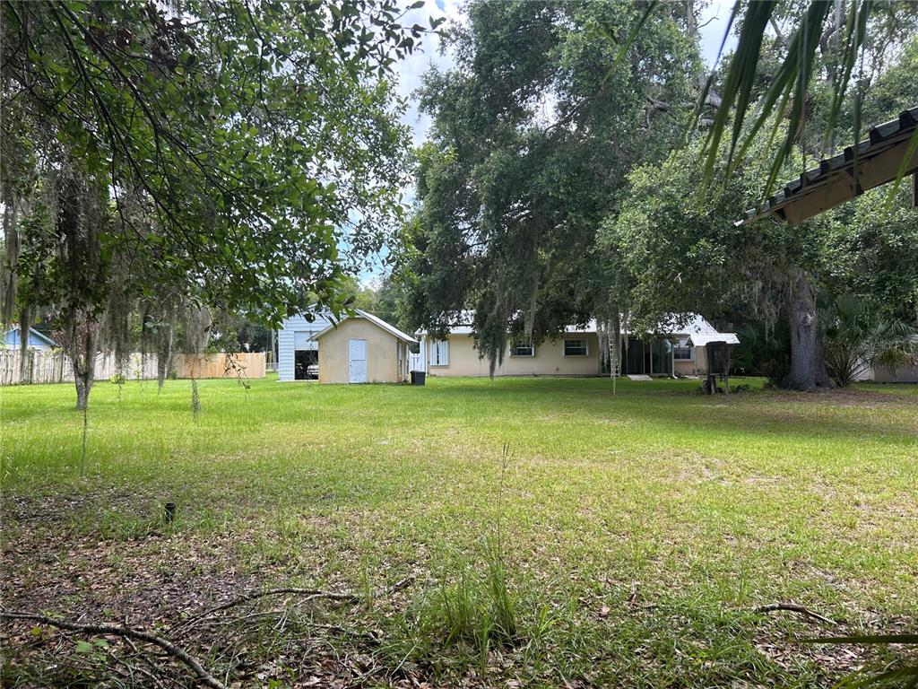 A backyard view features a house, a detached garage, and large trees on a lawn — 1671 FORD ROAD, MIMS, FL