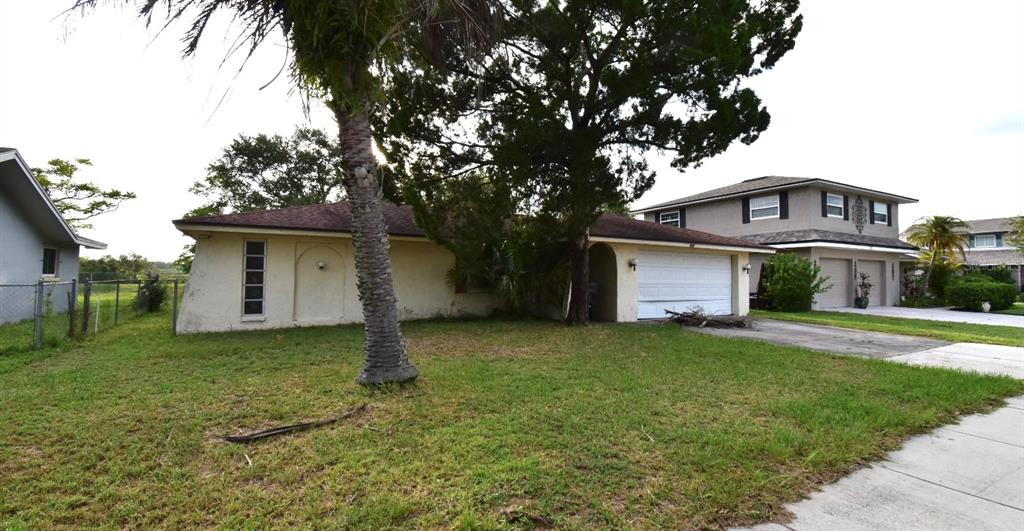 A single-story house with a white garage door and a large tree in the yard — 704 LEMONWOOD DRIVE, OLDSMAR, FL