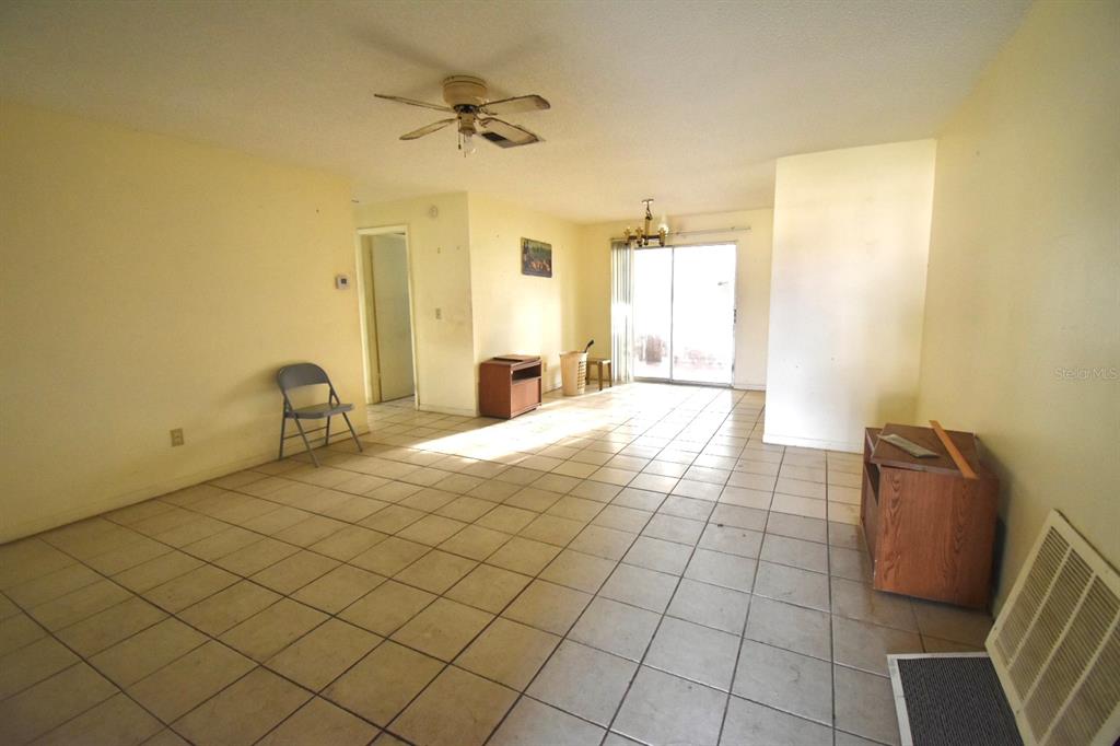 An empty living room with light-colored walls, tile flooring, a ceiling fan, and sliding doors — 704 LEMONWOOD DRIVE, OLDSMAR, FL