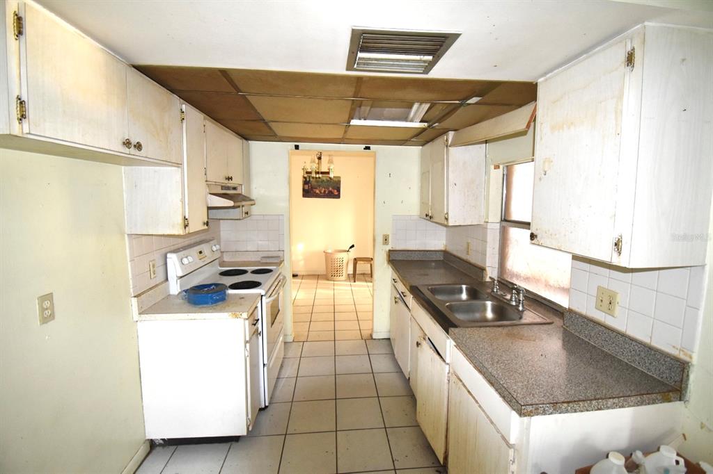 A dated kitchen features white cabinets, a double sink, and a tiled floor — 704 LEMONWOOD DRIVE, OLDSMAR, FL