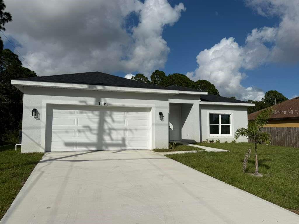 A single-story house with a white stucco exterior, a two-car garage, and a concrete driveway — 1121 COGAN DRIVE SE, PALM BAY, FL
