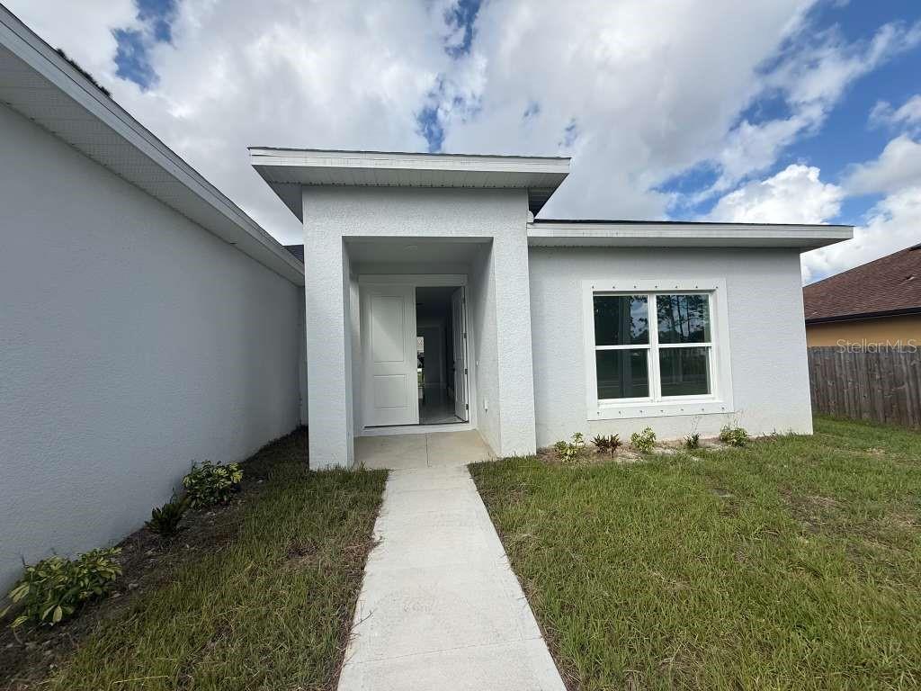 A concrete walkway leads to the white front entrance and window of a single-story house — 1121 COGAN DRIVE SE, PALM BAY, FL