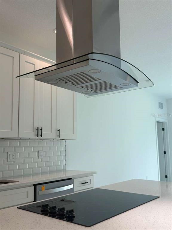 A kitchen features white cabinets, a glass-and-stainless steel range hood, and a black cooktop — 1121 COGAN DRIVE SE, PALM BAY, FL