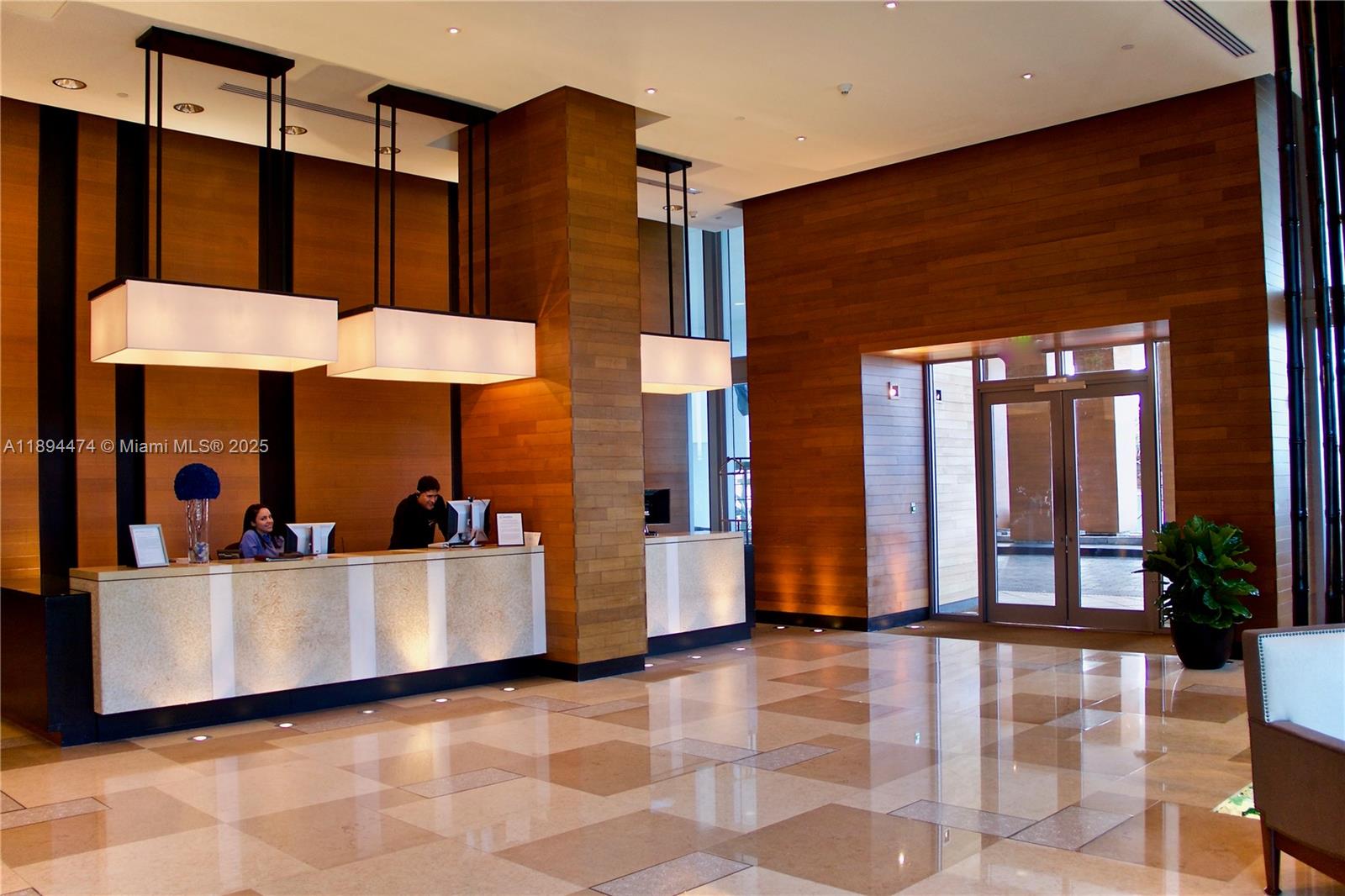A hotel lobby features a stone reception desk, wood-paneled walls, and hanging rectangular light fixtures — 6899 Collins Ave # 703, Miami Beach FL 33141, MIAMI BEACH, FL
