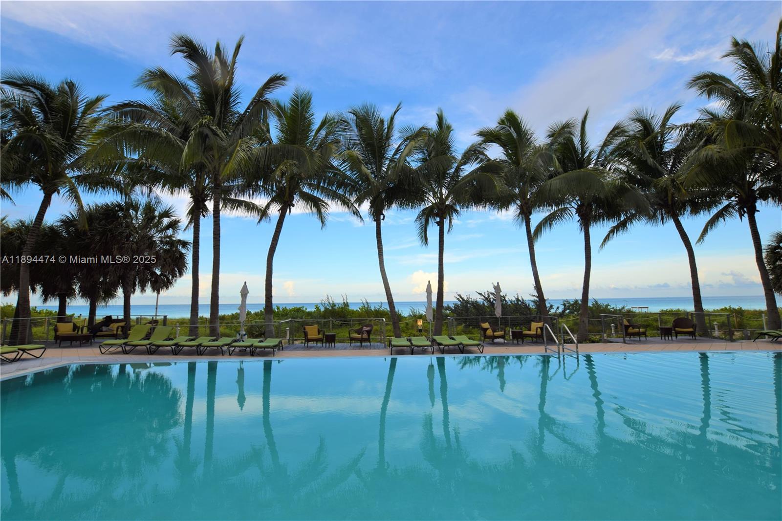 A swimming pool overlooks a beach lined with palm trees and outdoor lounge furniture — 6899 Collins Ave # 703, Miami Beach FL 33141, MIAMI BEACH, FL