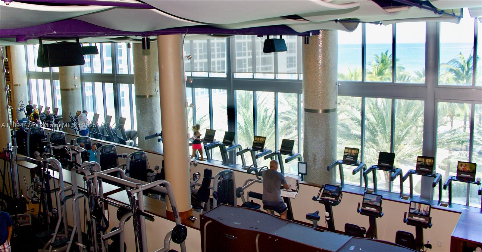 A fitness center features rows of exercise equipment, large windows, and views of the ocean — 6899 Collins Ave # 703, Miami Beach FL 33141, MIAMI BEACH, FL