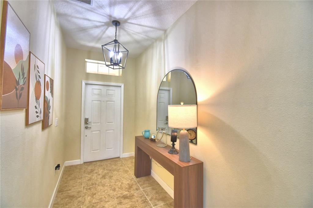 A bright entryway features a console table, a mirror, wall art, and a pendant light — 8958 SUGAR PALM ROAD, KISSIMMEE, FL