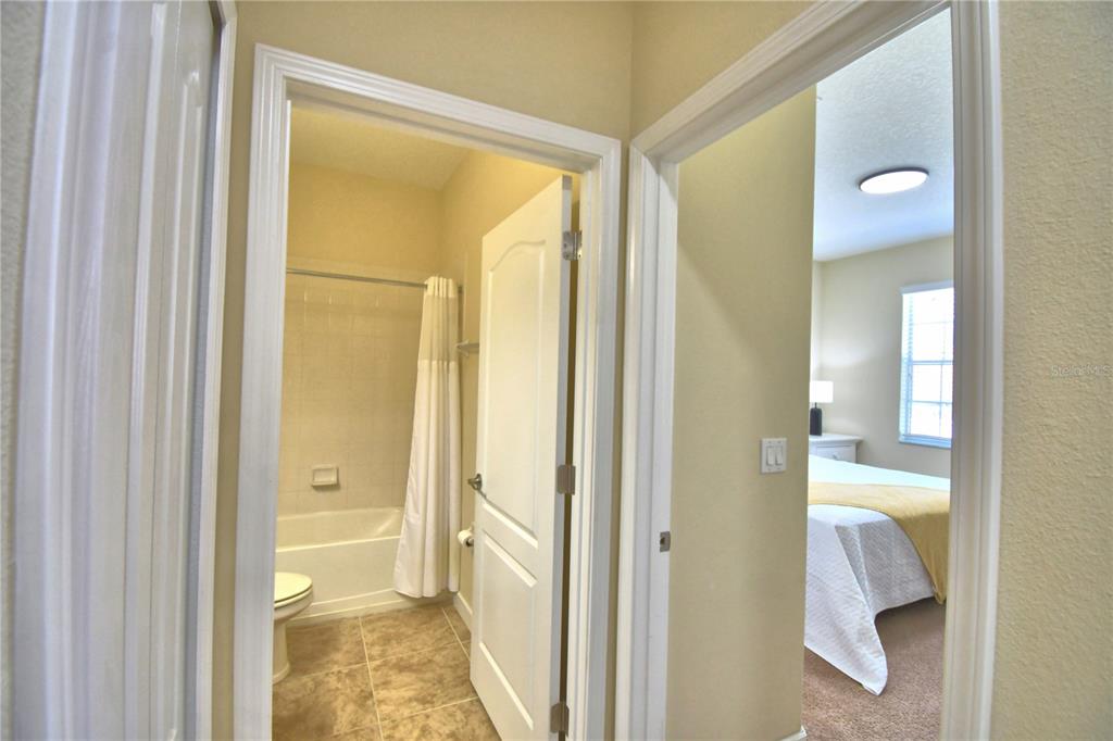 A view through two doorways shows a tiled bathroom and a carpeted bedroom — 8958 SUGAR PALM ROAD, KISSIMMEE, FL