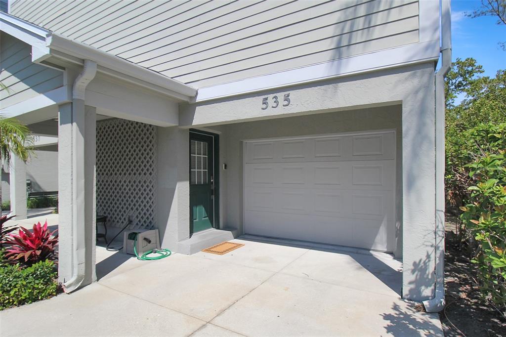 A beige two-story building exterior features a white garage door and a green entry door — 535 FOREST WAY, LONGBOAT KEY, FL