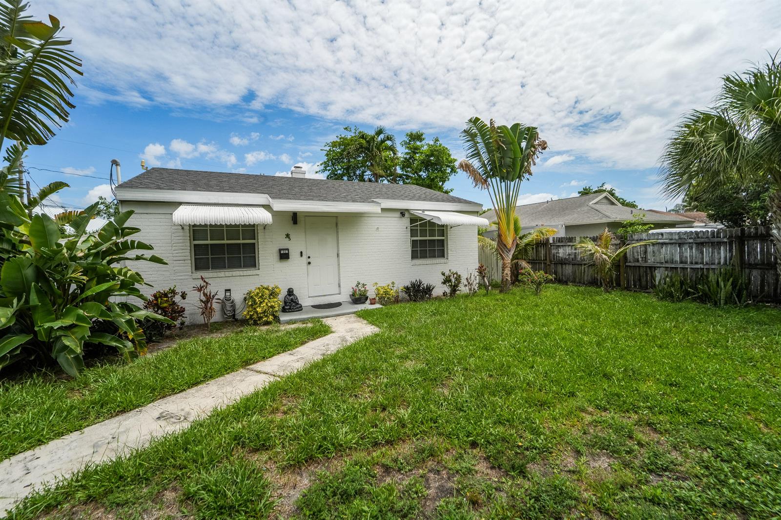 A white brick house with a front lawn, walkway, and tropical landscaping under a cloudy sky — 1007 Charles Street, West Palm Beach FL 33401, WEST PALM BEACH, FL
