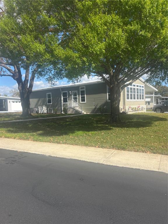 A single-story manufactured home with grey siding and large trees in the front yard — 105 FREEDOM COURT UNIT 30, PALM HARBOR, FL