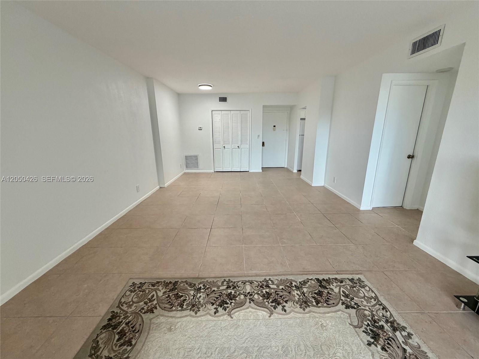 An empty room features light-colored tile flooring, white walls, and a patterned area rug — 4400 Hillcrest Dr # 308A, Hollywood FL 33021, HOLLYWOOD, FL