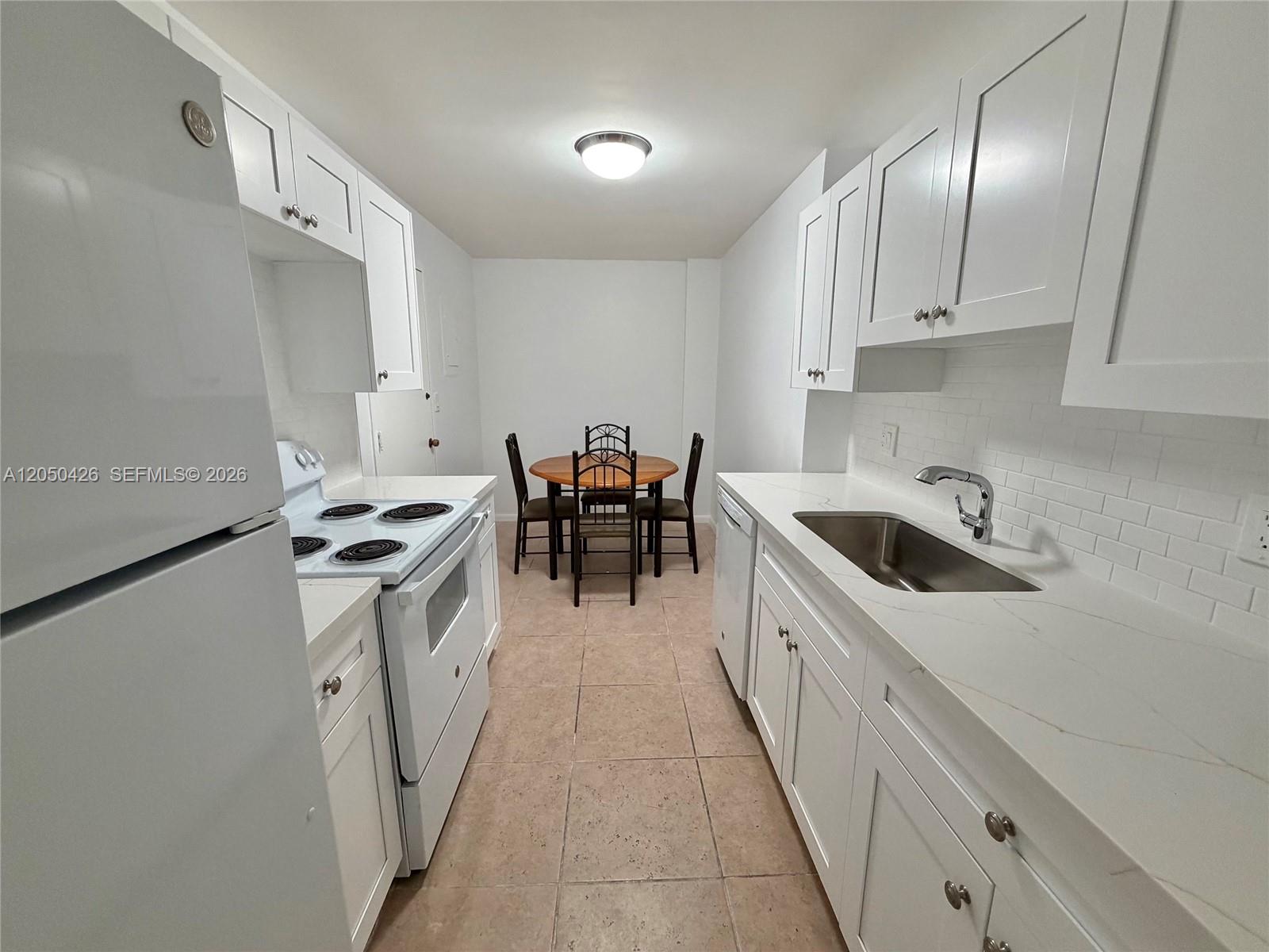 A galley kitchen features white cabinets, quartz countertops, a stainless steel sink, and dining area — 4400 Hillcrest Dr # 308A, Hollywood FL 33021, HOLLYWOOD, FL