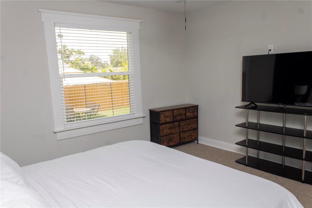A bedroom features a white bed, a small dresser, and a television on a metal stand — 2910 N OLA AVENUE, TAMPA, FL