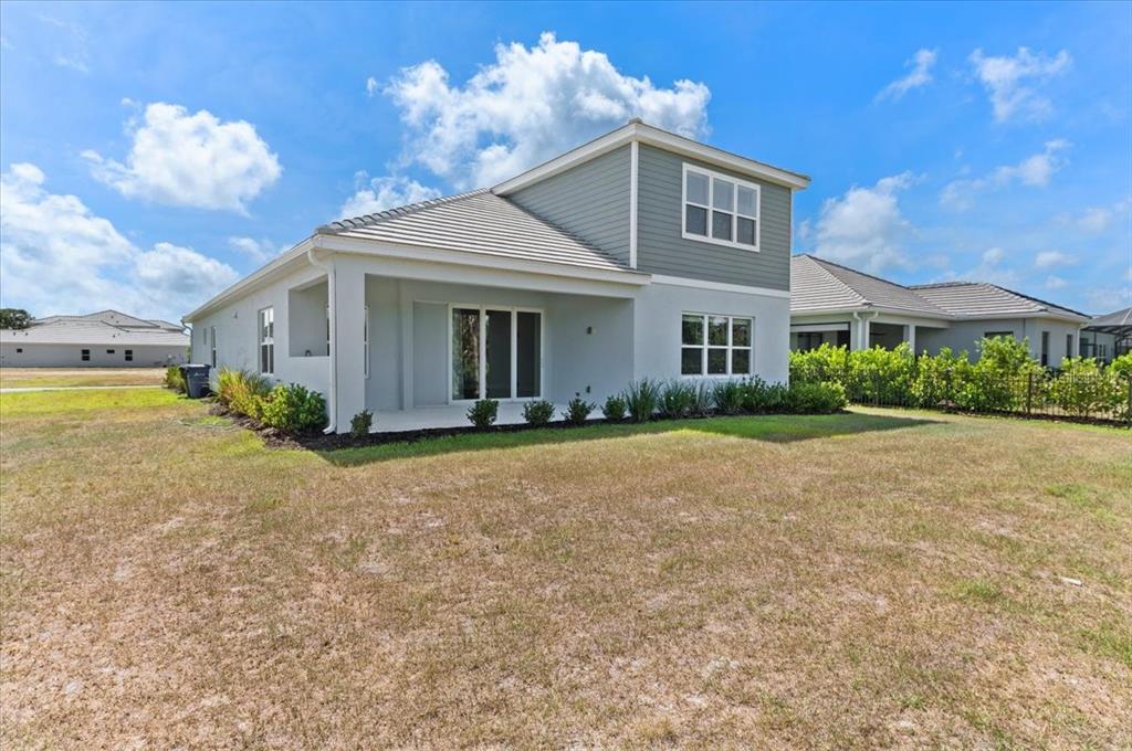 The rear exterior of a two-story house features a covered patio and a grassy yard — 10214 CRYSTAL ISLES CIRCLE, SARASOTA, FL