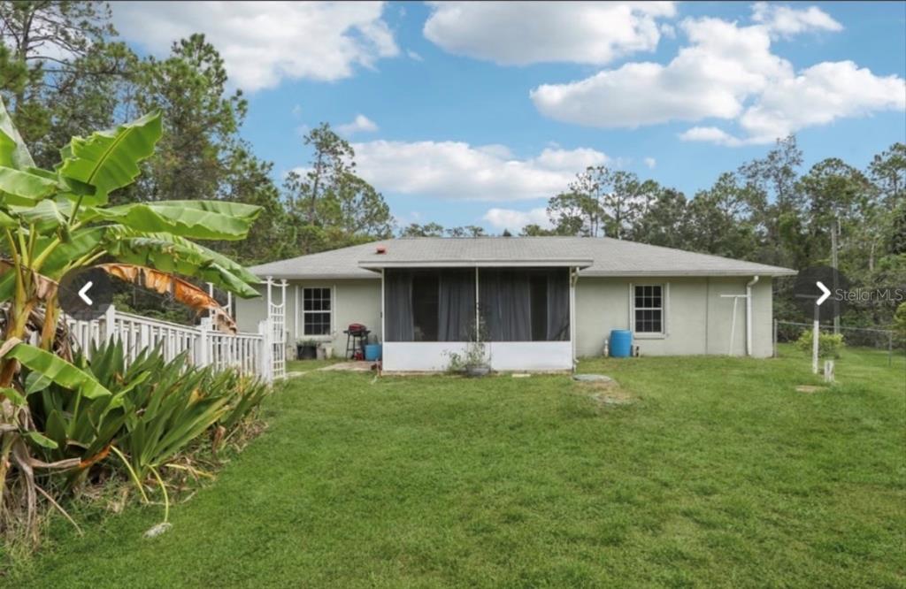 The rear exterior of a single-story house features a screened-in porch and a grassy yard — 1594 PAPAYA STREET, BUNNELL, FL