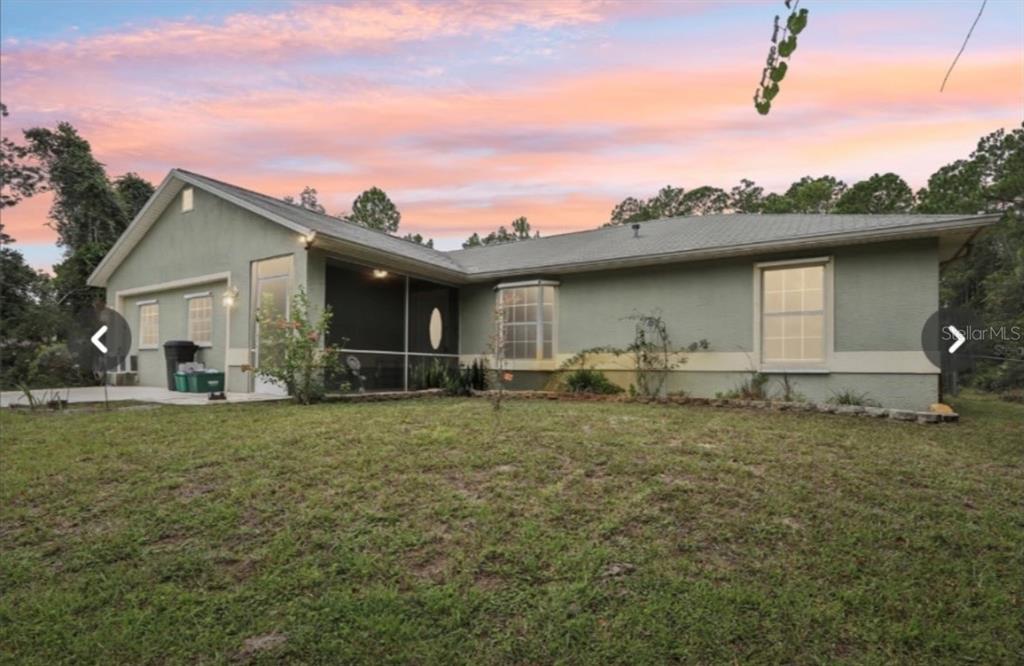 A single-story house with a screened-in porch and a green stucco exterior at sunset — 1594 PAPAYA STREET, BUNNELL, FL