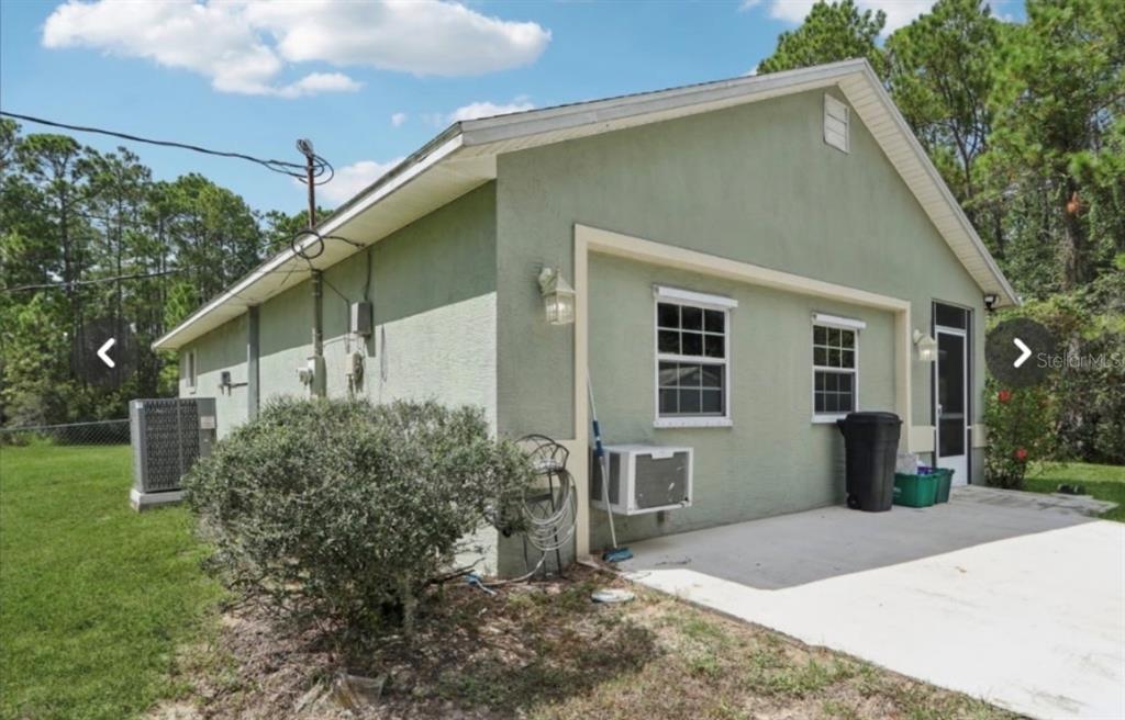 The exterior of a green stucco house features a concrete patio and a window unit — 1594 PAPAYA STREET, BUNNELL, FL