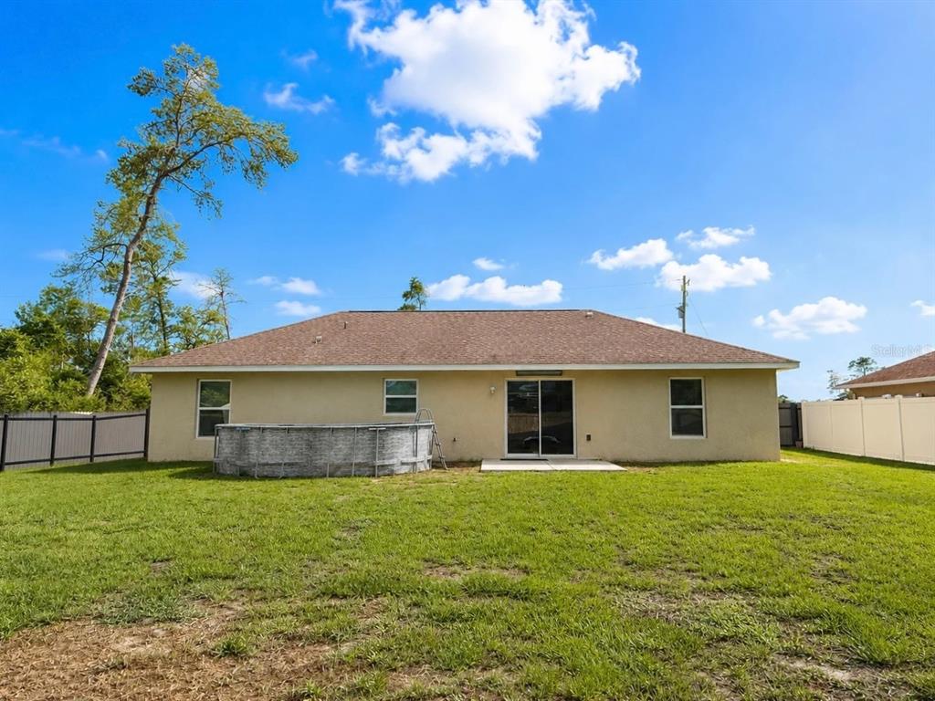 The exterior rear view of a house features a tan stucco facade and above-ground pool — 17023 SW 41ST AVENUE, OCALA, FL