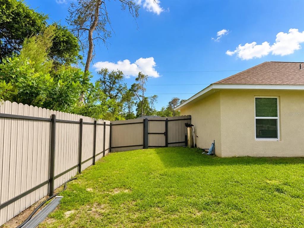 A backyard with a tan house, a white vinyl fence, and a gate — 17023 SW 41ST AVENUE, OCALA, FL